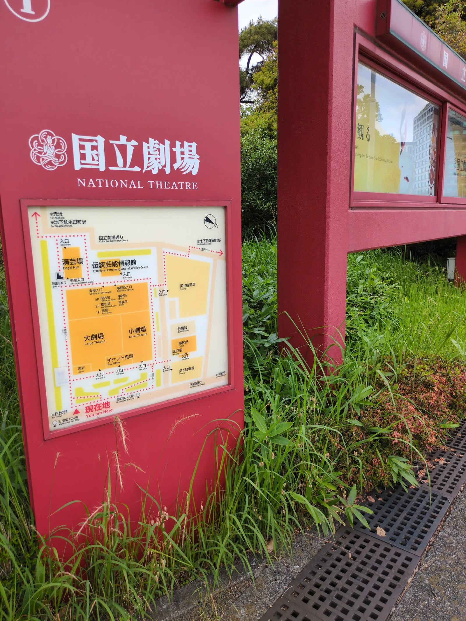 草に囲まれた国立劇場の赤い案内板。閉場中でも名前だけは鮮やかに残っている