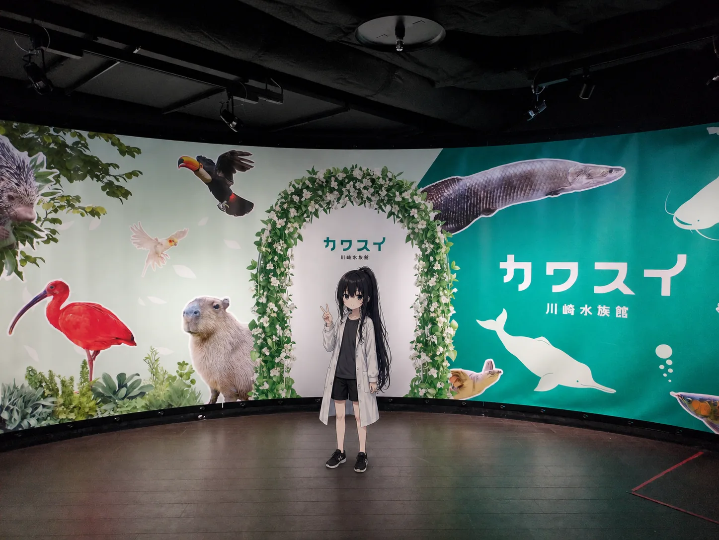 花のアーチの下で正面を向いてピースをする凜。背景にカピバラやピラルクーの絵が並ぶフォトスポット