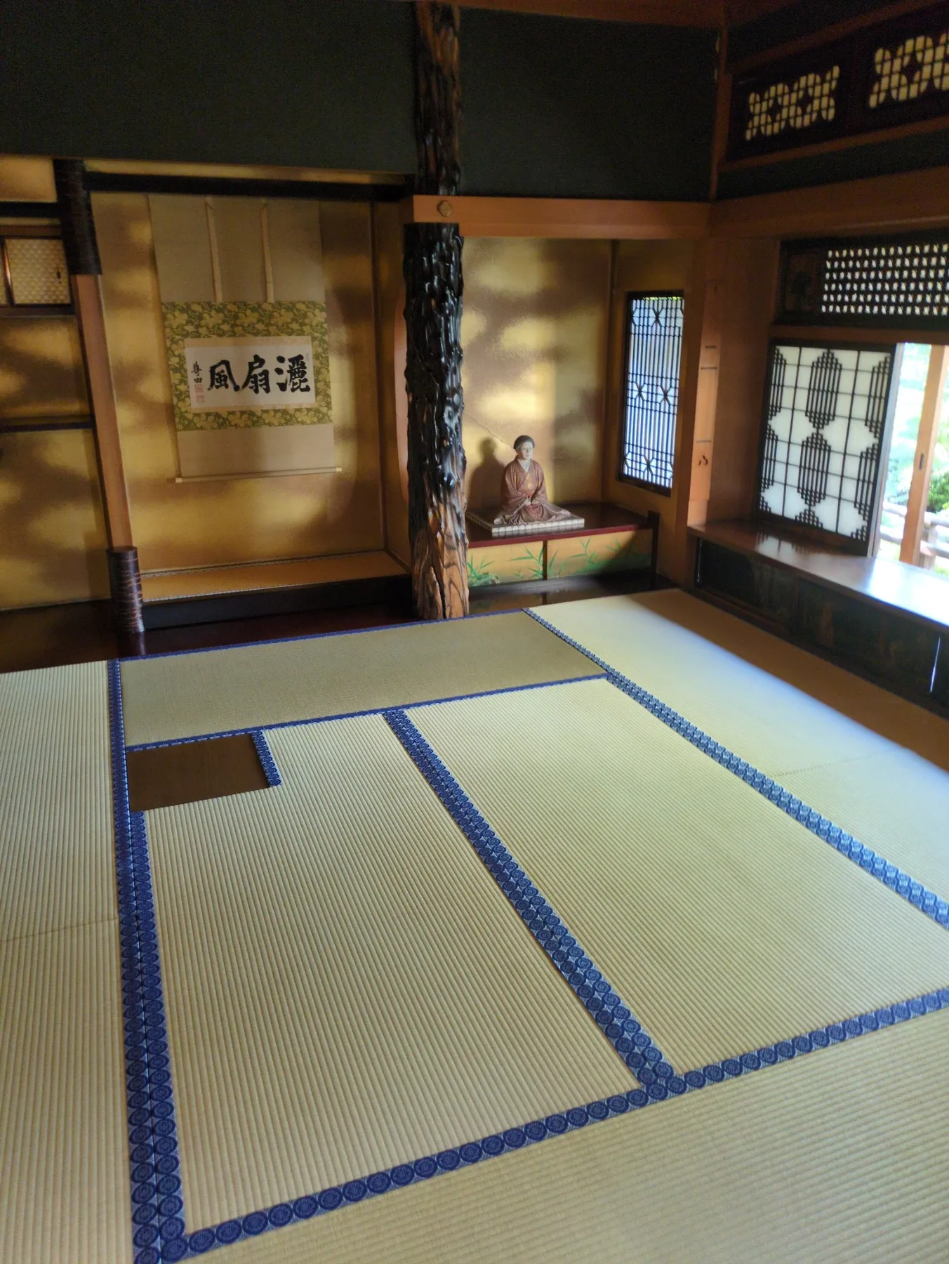 潮聲閣のお母様の居間。新しい畳、金色の壁、黒い床柱、床の間に座る人形が見える